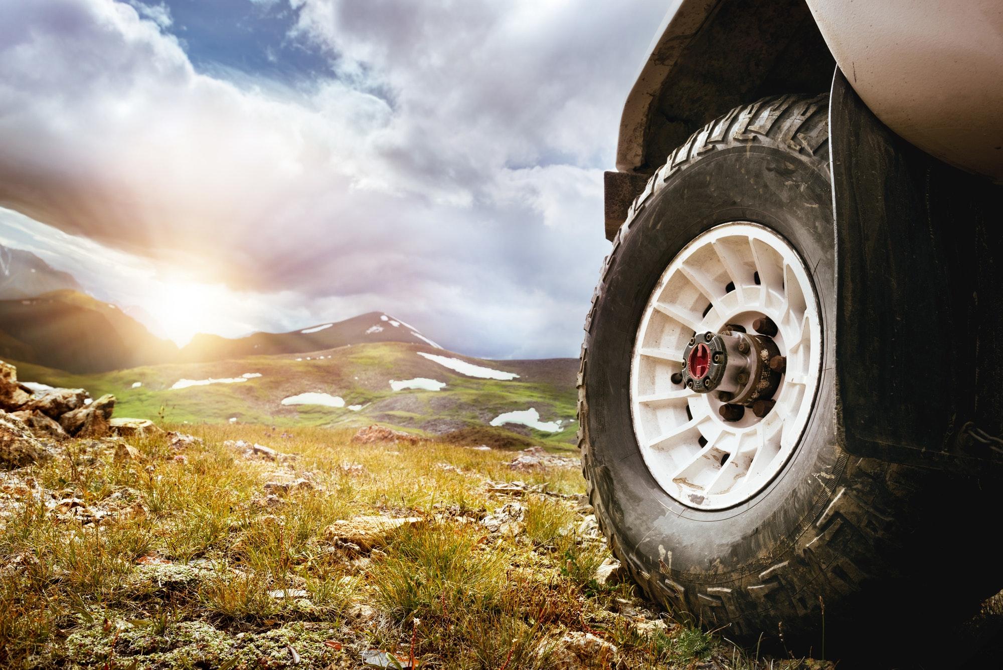 Big car wheel on mountains and sunset backdrop. Offroad 4x4 concept